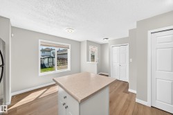 Central island with countertop, wood-finish flooring, light grey wall paint, modern ceiling lighting, and white baseboards - 