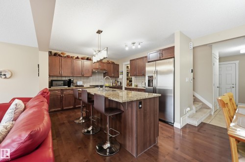 Kitchen featuring wood-finish flooring, wood cabinetry, stainless steel appliances, and a central island with a stone countertop - 1111 176 Street Sw, Edmonton, AB 