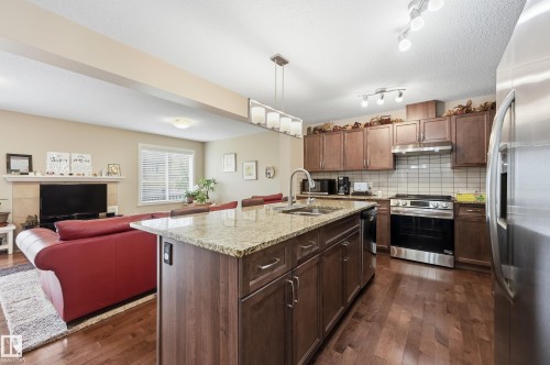 Kitchen island with a stone countertop and integrated sink, stainless steel appliances, wood-finish flooring, and a fireplace with a stone mantel - 1111 176 Street Sw, Edmonton, AB 