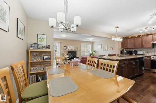 Open concept living area with wood-finish flooring, a kitchen island with stone countertop, dark wood cabinetry, and a stainless steel range with overhead hood - 1111 176 Street Sw, Edmonton, AB 