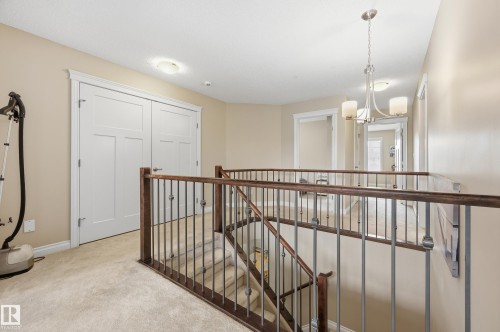 Upper level landing with plush carpeting, wood-finish railing with metal spindles, and a chrome chandelier - 1111 176 Street Sw, Edmonton, AB 