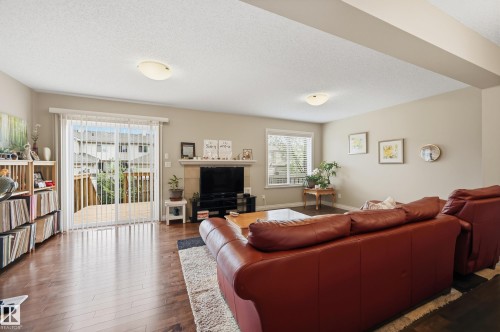 Living area featuring wood-finish flooring, a built-in fireplace with a stone surround, and light beige wall tones - 1111 176 Street Sw, Edmonton, AB 