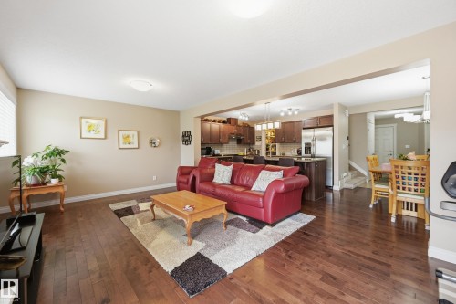 Rich wood-finish flooring throughout, open concept living area, kitchen with stainless steel appliances, dining area with chandelier, and light neutral wall colors - 1111 176 Street Sw, Edmonton, AB 