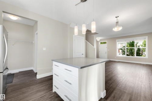 Kitchen island with stone countertop, suspended pendant lighting, wood-finish flooring, and a large window - 2125 24 Street Nw, Edmonton, AB 