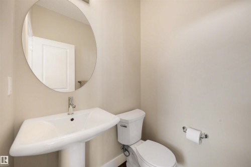 Pedestal sink with integrated basin, polished chrome faucet, round wall mirror, and a two-piece toilet - 2125 24 Street Nw, Edmonton, AB 