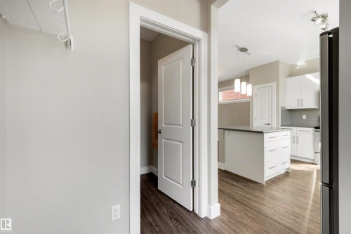 Kitchen with white cabinetry, dark countertop island, pendant lighting, and wood-finish flooring - 2125 24 Street Nw, Edmonton, AB 