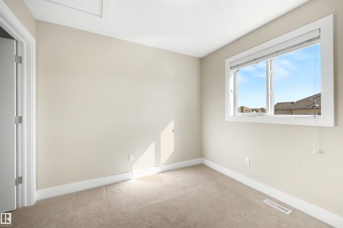 Neutral wall color with plush carpeting, featuring a window with white trim and a white paneled door - 2125 24 Street Nw, Edmonton, AB 