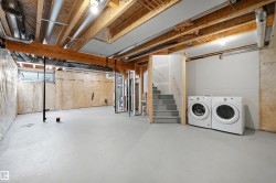 Unfinished lower level featuring exposed wood joists, concrete flooring, perimeter wall insulation, and a utility staircase - 