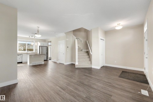 Open-concept living space with wood-finish flooring, a kitchen island, stainless steel appliances, and a carpeted staircase - 2125 24 Street Nw, Edmonton, AB 