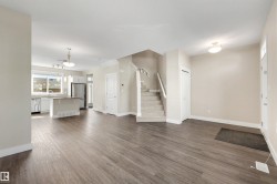 Open-concept living space with wood-finish flooring, a kitchen island, stainless steel appliances, and a carpeted staircase - 