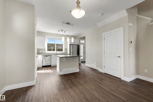 Open-concept living space with wood-finish flooring, a kitchen island, stainless steel appliances, and ceiling-mounted lighting - 2125 24 Street Nw, Edmonton, AB 