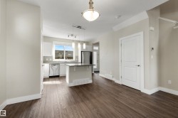 Open-concept living space with wood-finish flooring, a kitchen island, stainless steel appliances, and ceiling-mounted lighting - 