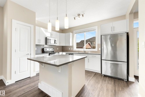 Kitchen featuring white cabinetry, stainless steel appliances, a center island with countertop, wood-finish flooring, and a subway tile backsplash - 2125 24 Street Nw, Edmonton, AB 