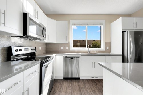 Contemporary kitchen featuring white cabinetry, gray countertops, stainless steel appliances, a tile backsplash, and wood-finish flooring - 2125 24 Street Nw, Edmonton, AB 