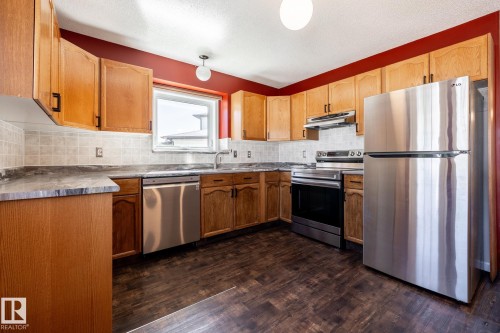 Kitchen featuring wood cabinetry, stainless steel appliances, a tiled backsplash, and dark wood-finish flooring - 89 Ozerna Road Nw, Edmonton, AB 