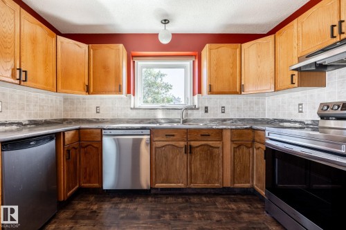 Kitchen featuring wood-finish cabinetry, stainless steel appliances, tiled backsplash, and dark countertops - 89 Ozerna Road Nw, Edmonton, AB 