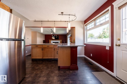 Built-in kitchen island with stone-finish countertop, wood cabinetry, and stainless steel refrigerator - 89 Ozerna Road Nw, Edmonton, AB 