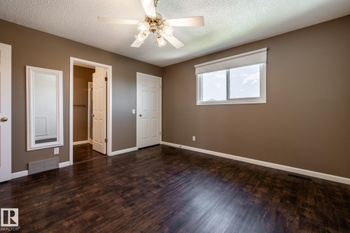 Dark wood-finish flooring, white trim, window with roller shade, ceiling fan with integrated lighting, and a closet with bifold doors - 89 Ozerna Road Nw, Edmonton, AB 