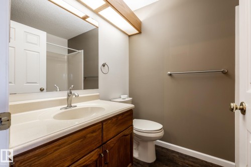 Wood-finish vanity with a single basin sink, wall-mounted mirror, and white toilet - 89 Ozerna Road Nw, Edmonton, AB 
