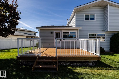 Wood-finish deck with white railing, featuring a two-step entry and expansive green lawn - 89 Ozerna Road Nw, Edmonton, AB 