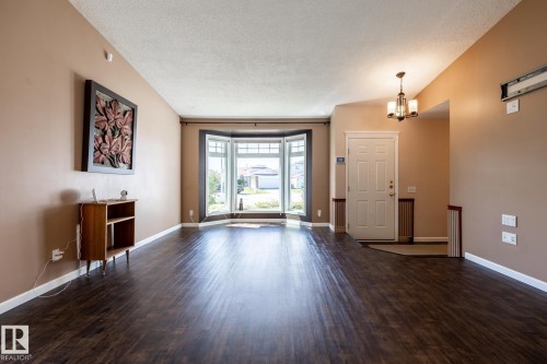 Dark wood-finish flooring, bay window with multiple panes, entryway with panel door, decorative chandelier, and neutral wall paint - 89 Ozerna Road Nw, Edmonton, AB 