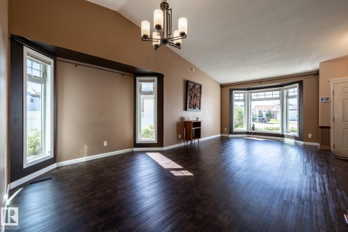 Spacious room with dark wood-finish flooring, vaulted ceiling, and a prominent bay window - 89 Ozerna Road Nw, Edmonton, AB 