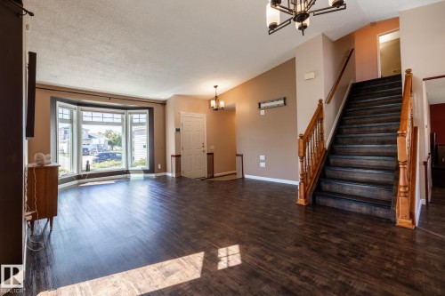 Expansive main living area featuring dark wood-finish flooring, a bay window with multiple panes, a prominent staircase with wood banister, and a decorative chandelier - 89 Ozerna Road Nw, Edmonton, AB 