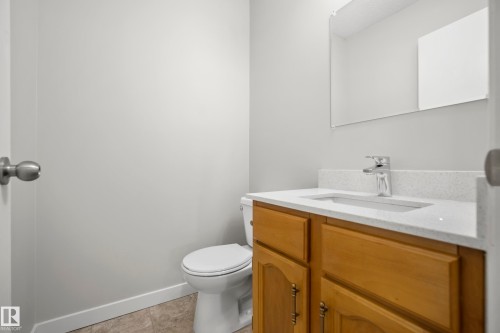 Light wood-finish vanity with a white countertop and undermount sink, chrome faucet, and rectangular wall-mounted mirror - 3173 139 Avenue Nw, Edmonton, AB 
