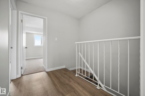 Wood-finish flooring with white baseboards, a white metal stair railing, and a light gray wall finish - 3173 139 Avenue Nw, Edmonton, AB 