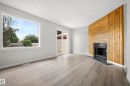 Spacious interior featuring a fireplace with a wood-paneled accent wall, large picture window, sliding glass patio door, and wood-finish flooring - 3173 139 Avenue Nw, Edmonton, AB 