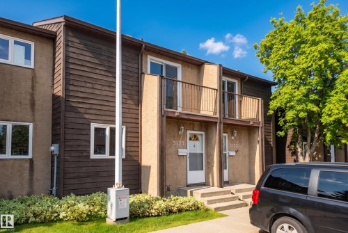 Exterior featuring stucco and horizontal plank siding, multiple windows with white frames, a second-story balcony with metal railing, and concrete steps leading to the entrance - 3173 139 Avenue Nw, Edmonton, AB 