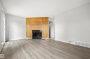 Wood-finish flooring, fireplace with a black surround, wood panel accent wall, light gray wall paint, and a sliding glass door - 3173 139 Avenue Nw, Edmonton, AB 
