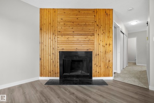 Wood-finish flooring, wood-paneled accent wall, and a black fireplace with a tiled hearth - 3173 139 Avenue Nw, Edmonton, AB 