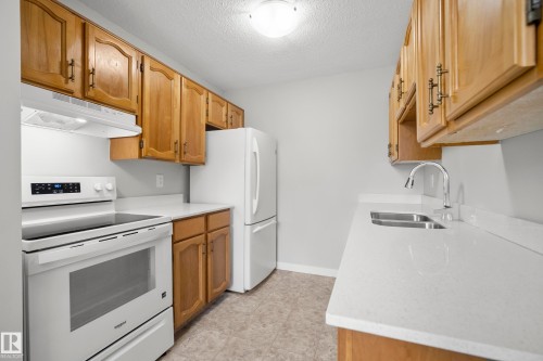 Kitchen featuring wood cabinetry, white countertops, stainless steel double basin sink, chrome gooseneck faucet, and white appliances - 3173 139 Avenue Nw, Edmonton, AB 