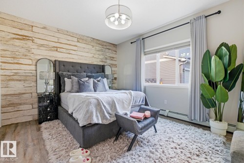 Accent wall with wood-finish paneling, contemporary chandelier, large window with natural light, and wood-finish flooring - #155 1818 Rutherford Rd Sw, Edmonton, AB 
