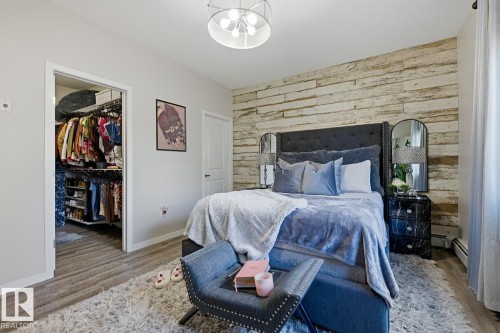 Bedroom featuring a wood-finish accent wall, built-in closet organization system, and wood-finish flooring - #155 1818 Rutherford Rd Sw, Edmonton, AB 