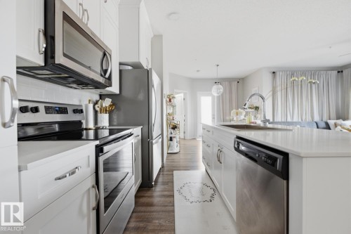 White cabinetry with stainless steel appliances, solid surface countertops, and wood-finish flooring - #155 1818 Rutherford Rd Sw, Edmonton, AB 