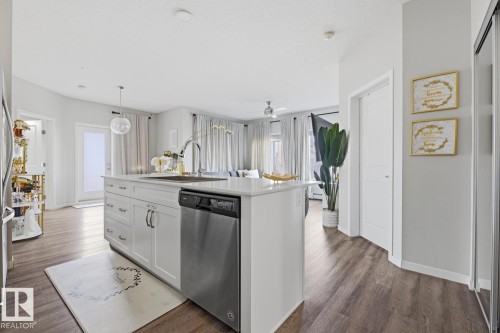 Kitchen island with white cabinetry, integrated stainless steel dishwasher, and a single-basin sink with a gooseneck faucet - #155 1818 Rutherford Rd Sw, Edmonton, AB 