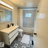 Bathroom featuring a modern floating vanity with an integrated sink and matte black faucet, geometric black and white floor tiling, and a tiled shower-tub combination with a rectangular window - 