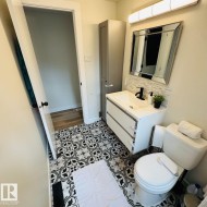 Bathroom featuring patterned floor tiles, a white vanity with integrated sink, a rectangular mirror, a toilet, and a tall storage cabinet - 