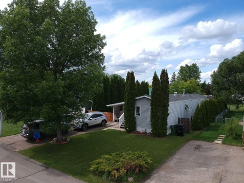 Property exterior featuring light gray siding, a well-maintained lawn, privacy trees, and a paved driveway - 8 The Parkway Northwest, Edmonton, AB - Outdoor