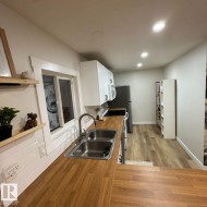 Kitchen featuring wood-finish countertops, subway tile backsplash, white cabinetry with contemporary hardware, a double basin stainless steel sink with a gooseneck faucet, and recessed ceiling lighting - 