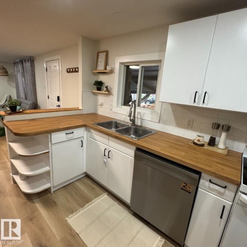 Kitchen featuring wood-finish countertops, white cabinetry with black hardware, stainless steel double basin sink, and white subway tile backsplash - 8 The Parkway Northwest, Edmonton, AB - Indoor Photo Showing Kitchen With Double Sink