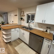 Kitchen featuring wood-finish countertops, white cabinetry with black hardware, stainless steel double basin sink, and white subway tile backsplash - 