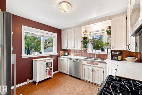 Kitchen featuring wood-finish flooring, white cabinetry, stainless steel dishwasher, and a pressed copper tile backsplash - 10943 72 Avenue Nw, Edmonton, AB 