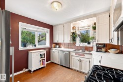 Kitchen featuring wood-finish flooring, white cabinetry, stainless steel dishwasher, and a pressed copper tile backsplash - 