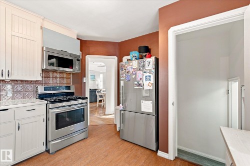 White cabinetry, stainless steel appliances, patterned backsplash, wood-finish flooring, and a pantry with shelving - 10943 72 Avenue Nw, Edmonton, AB 