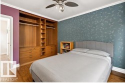 Hardwood flooring, crown molding, ceiling fan with light fixture, built-in wood-finish cabinetry, and patterned accent wall - 