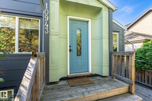 Front entry with a light blue door, decorative green stucco surround, and a natural wood-finish deck - 10943 72 Avenue Nw, Edmonton, AB 