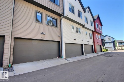 Exterior townhome elevation featuring horizontal siding in a neutral tone, contemporary dark gray garage door, and modern windows with dark frames - #99 1010 Rabbit Hill Rd Sw, Edmonton, AB 